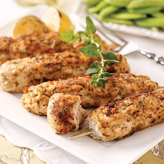Chicken spiedini skewers with garnish on white plate with fork and lemon in background